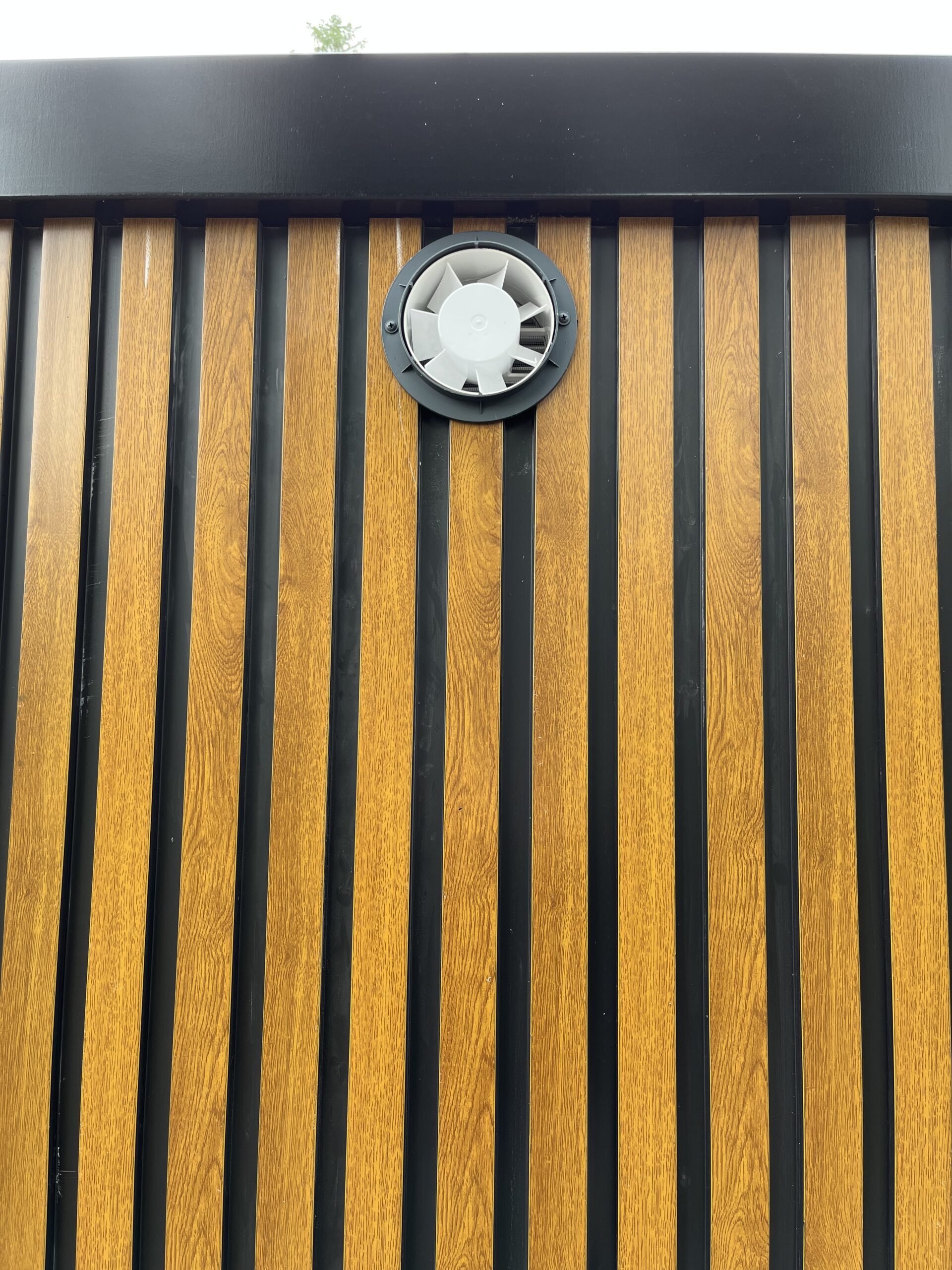 Elektrische ventilatie aan de achterzijde van een duo mobiele douchecabine unit met pvc houtlook afwerking aan de buitenkant