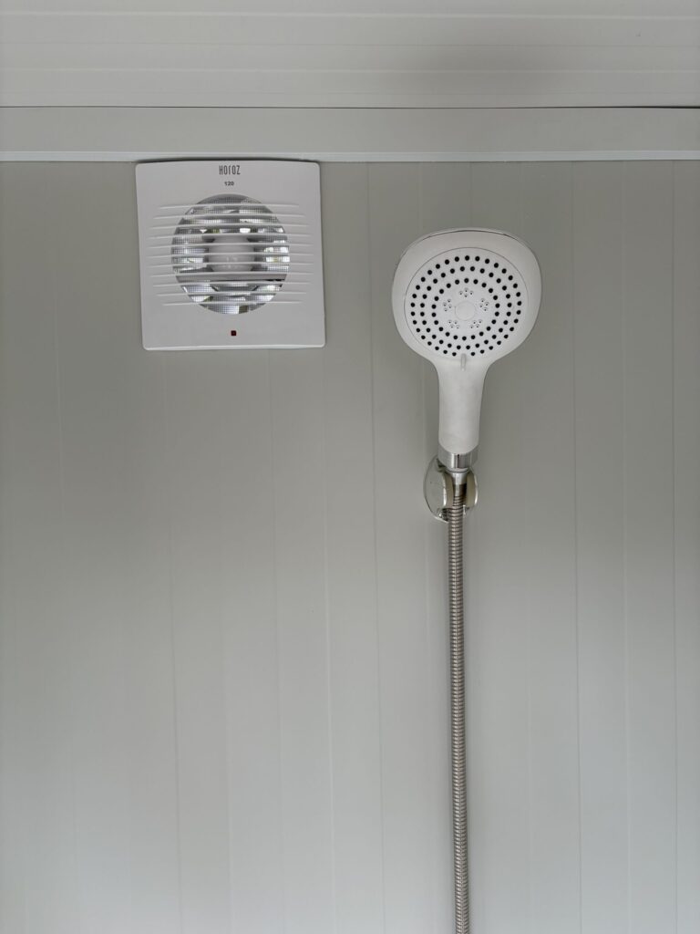Binnenzijde van een duo mobiele douchecabine unit met douchekop en ventilatie zichtbaar