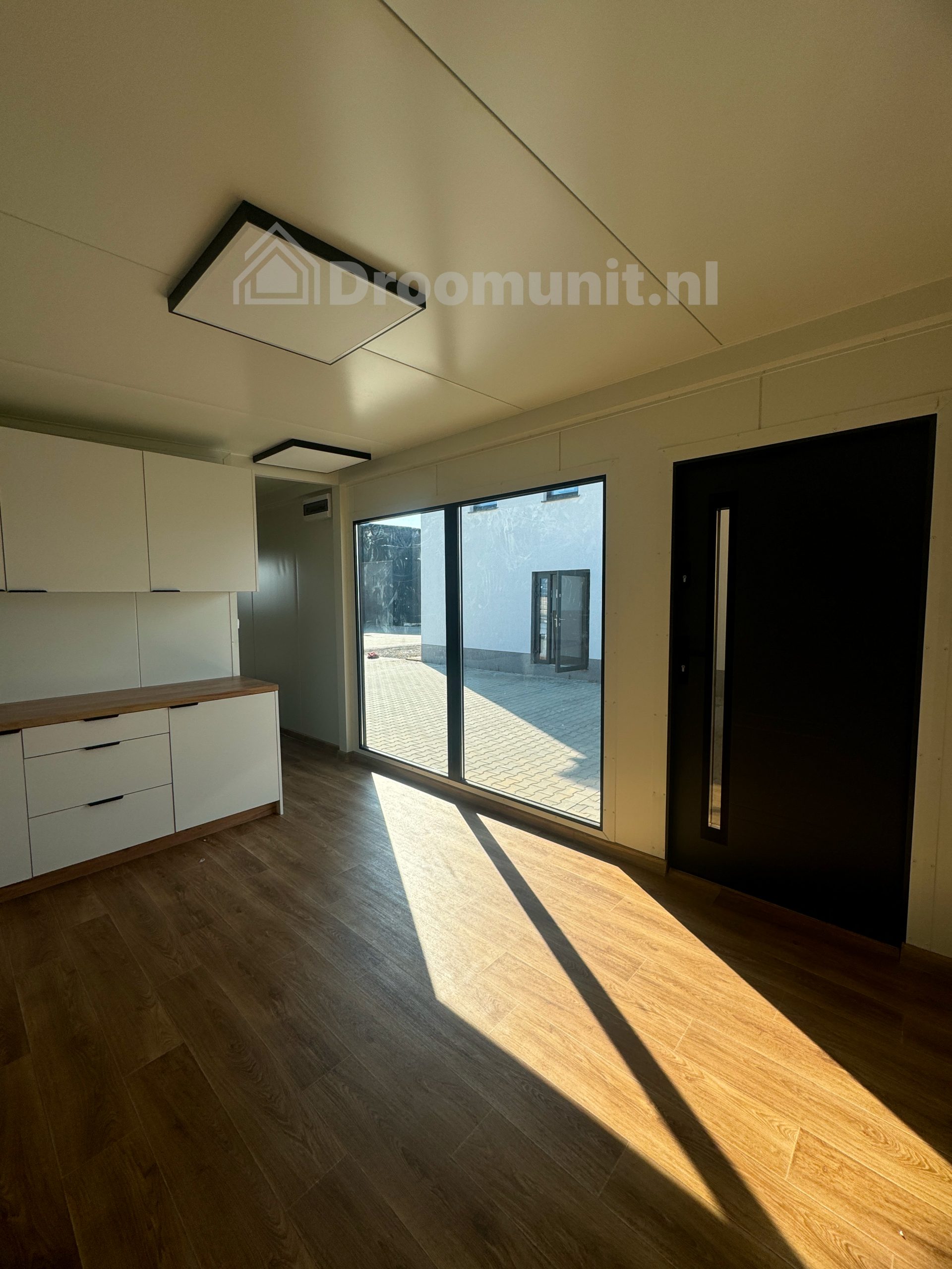 Leefruimte met keuken, kozijn en voordeur in luxe mobiele prefab woonunit Emmy met 1 slaapkamer, afmeting 1000x300
