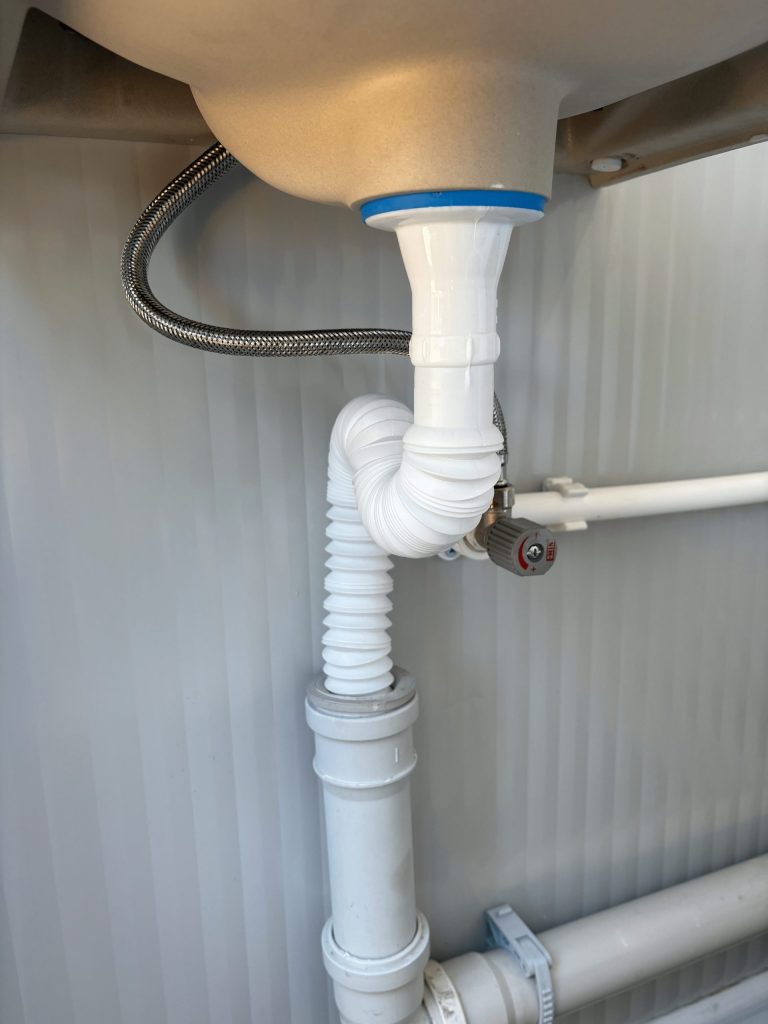 Close-up van leidingwerk bij wastafel in een mobiele toilet unit